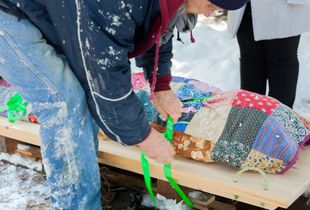 Quilt-covered body is secured to a sled for transport to the grave site.