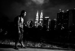 A homeless man walks to his shelter in the dead of night against the background of metropolitan city of Kuala Lumpur.