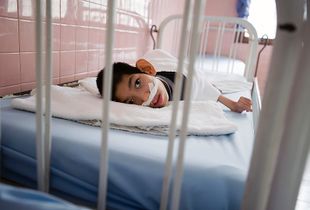 A physically and mentally disabled child lies in a hospital bed.