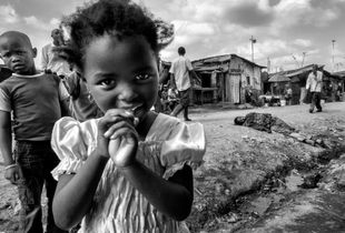 © Tony Corocher - Contrasts: Curiosity & diffidence, desperation & indifference. Through the streets of Mathare Slum (Nairobi). The contrast between the innocent beauty of the young girl, the vivid diffidence of the boy behind her, the finality of the desperation shown by the man on the ground behind her and the indifference of the people passing by… this is the ensemble of feelings that runs thro