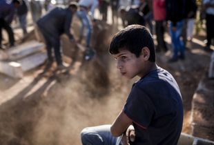 A young boy looks on as mourners cover with soil the grave of a Kurdish Protection Unit (YPG) fighter who died during fighting in the besieged Syrian border town of Kobane, in the town of Suruc, Sanliurfa province, Turkey on November 6, 2014.