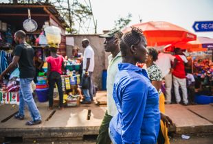 A man and woman walk past busy market stalls in Freetown.