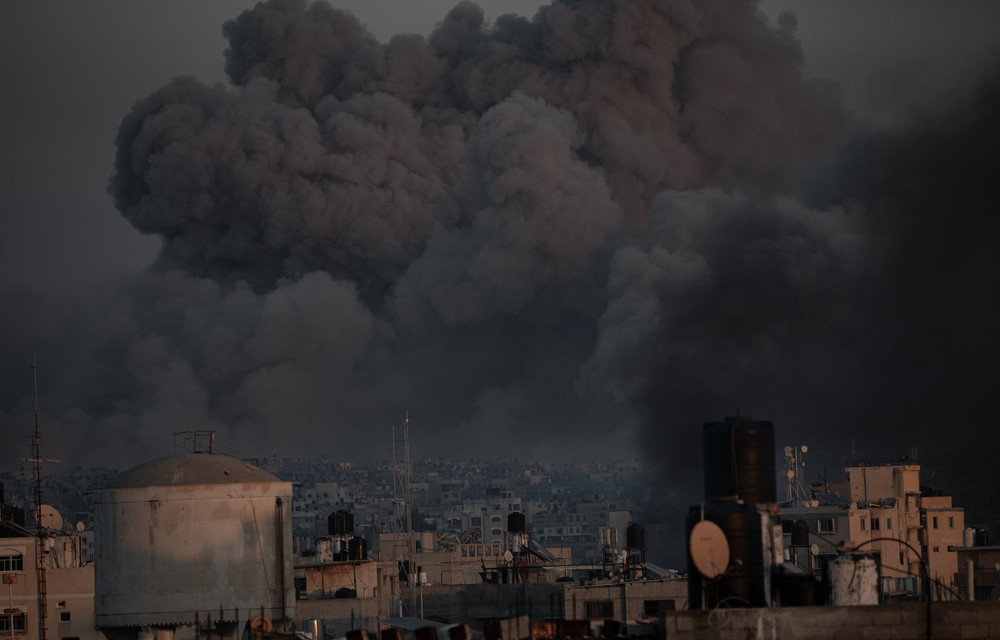 Khan Younis Vanishes Under Fire. When the Horizon Turns to Ash. In this tragic moment, thick plumes of smoke rise from the city of Khan Younis, in southern Gaza, following a brutal airstrike that turned entire neighborhoods into ruins. The bombings spared neither homes, schools, nor hospitals, as if the city itself is being erased from existence under the weight of the bombs. The horizon, once a symbol of life, is now covered in ash and smoke, as if the sky bears witness to the ongoing annihilation. This image captures the sheer brutality of the relentless war, where cities are left to disappear in the face of global silence. It is a silent scream from beneath the rubble, unheard amid the smoke of war, yet throbbing with pain and the will to survive. © Abdelrahman Alkahlout