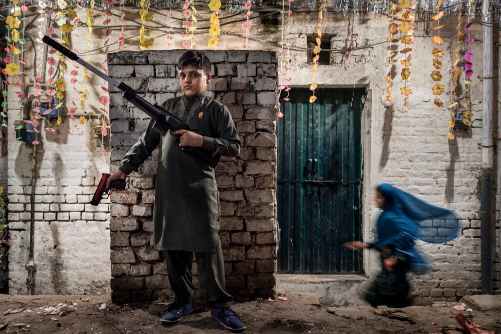 On the eve of religious celebration, a gracious blue shadow floats by a boy boasting his toy guns.