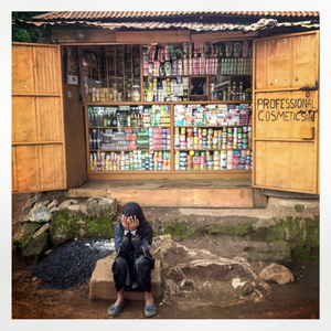 A young woman holds her head in her hands as she sits oin front of a shop in Kibera. The Kibera slum is the largest slum in Nairobi with around half a million inhabitants.