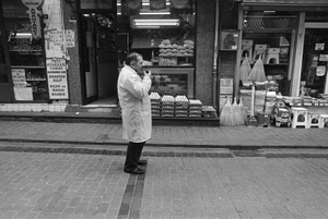 A shopkeeper drinks a glass of tea in while standing in front of his shop.