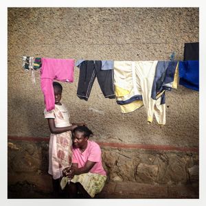 Two girls sit beneath clothes hanging on a washing line in Kibera. The Kibera slum is the largest slum in Nairobi with around half a million inhabitants.