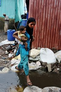 A lady caaries her child to a Polio booth crossing overflooded streets in Rafiq Nagar slums, Mumbai, Maharashtra