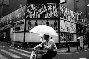 A man on a bike pass in front of the avertissement for men's bar in Kabukicho
