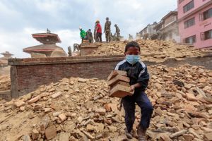 A boy joins relief and recovery efforts, carrying bricks from a temple destroyed by the  2015 Nepal earthquake.