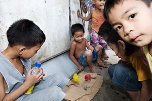 Kids are trying to get two chicks (one dyed red) to eat a baby rat.