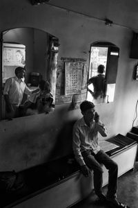 The Barber - One customer passes time on the phone while another waits by the door for their turn.