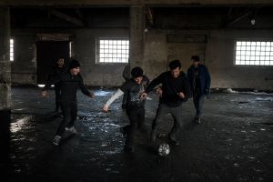 Refugees trying to keep warm and to have fun playing football in an abandoned warehouse