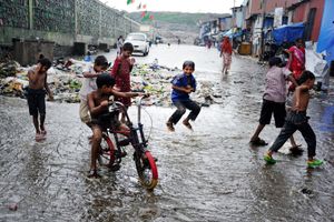 Children play around garbage and over flooded drain water in the slums of Rafiq Nagar, Mumbai, India