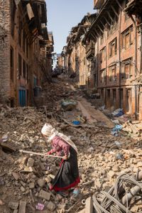 An elderly woman uses a garden hoe to search through the rubble of a house destroyed by the 2015 Nepal earthquake.