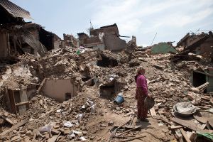 A woman waiting in the debris of her collapsed house to collect her belongings.