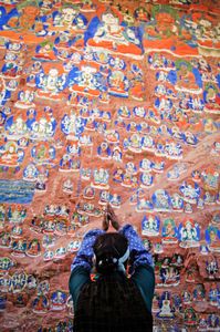 Scene along the Lingkor. The Lingkor is a devotional route followed by pilgrims that encompasses much of Lhasa, Tibet. It includes rock paintings, prayer wheels, sangkangs (incense burners), and many other, more secular sights. This woman is praying in front of old rock paintings. Photographed on 29 June 2005 © Forest McMullin