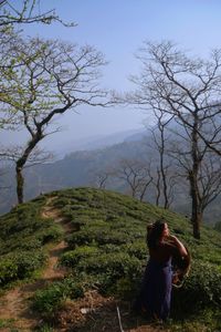 Tea picker readjusts her headgear with the plantation trail in the background.