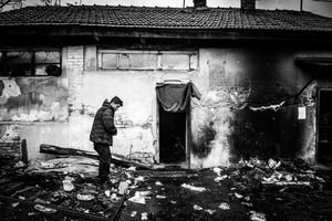 Man at the front of abandoned building, which is his temporary shelter, at the back the main train station. Belgrade, Serbia.