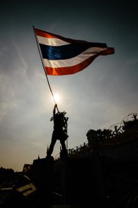 An anti-Government protester standing on top of concrete barriers and waving the Thai national flag in front of Government House in Bangkok. Thailand.