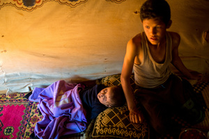 Bekaa Valley, LEBANON, September 5, 2014:  Syrian refugee Jassem, 12, watches over his little brother, 3, as he sleeps in their tent in an informal settlement in Lebanon's Bekaa Valley. Jassem and his parents fled Syria in late 2011. They have been living in makeshift shelters ever since. Today their papers have expired, resulting in them being stuck, unable to return to Syria if they wanted to, a