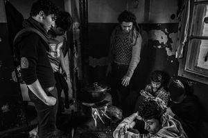 Inside abandoned building, migrants prepare meal together. Belgrade, Serbia.
