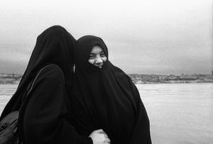 Two women, dressed in Chadors, laugh as they pose for a photo on the shore of the Golden Horn.