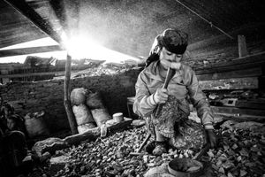 A woman crushing rocks into gravel with a hammer; this material is needed for constructing houses. It is hard and laborious work, which they do for several hours every day. Barpak, in Gorkha District, the epicenter of the earthquake of 25 April 2015.