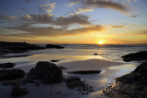 Looking at the ocean / A seascape of the rugged coast on the Atlantic Ocean, along the Cape Peninsula, South Africa. A double long exposure with rocks and water in the foreground and a solitary person looking at the sunset and the setting sun in the cloudy sky in the background.