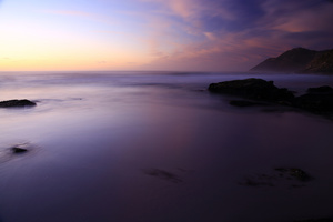 Silk / A double long exposure on the Atlantic Ocean with blurry water, rocks and sand in the foreground and mountains, clouds and sky at sunset in the background. Relax ...