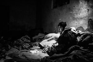 Stranded refugee inside derelict warehouse where is cold, so people have to use blanket to warm themselves, Belgrade, Serbia.