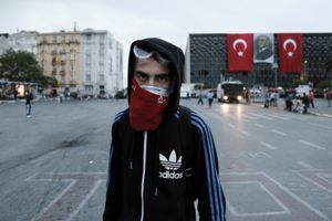 A demonstrator with a kerchief over his face poses in front of the former Atatürk Cultural Center decorated with Turkish flags and a portrait of Mustafa Kemal Ataturk, the founder of modern Turkey, in Istanbul, Turkey, Wednesday, June 12, 2013.