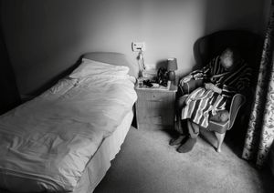 After getting up late my father sits and sleeps in his dressing gown as he waits to be dressed and given his medication by one of the nurses.