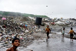 Children play around garbage and over flooded drain water in the slums of Rafiq Nagar, Mumbai, India
