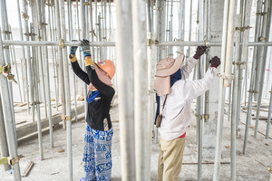 Keo Sokem 28 from Pursat Province and Khuon Tout 36 from Battambang Province work in unison to tighten scaffolding which is used to support the understide of a new level on a house construction.