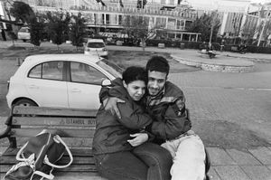 A couple, sitting on a bench, cuddle each other.