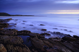On the rocks / A seascape of the rugged coast on the Atlantic Ocean, along the Cape Peninsula, South Africa. A double long exposure with rocks and blurred waves in the foreground and the sky at sunset in the background.