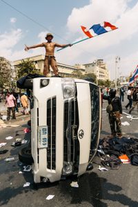 An anti-government protesters carrying a Thai flag stands on top of an overturned ambulance following clashes between demonstrators and police.