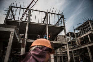 Oung Vanak 45 from Srey Rieng Province walks past a house under construction whilst male workers look down from the building.