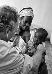 Unlike the heartbreaking images of the severely malnourished, this healthy family represents the future of Africa. With clean water, education and healthcare, their future holds promise. This adoring mother nestles her youngest of three. Somehow you know the doctor is smiling, enjoying a shared moment of understanding with  another parent.                                       © Lola Reid Allin