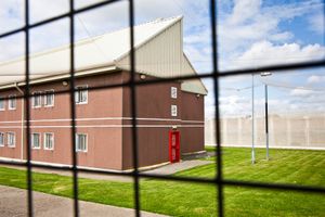 Looking through a security fence at a red fire security door at the end of one of the residential wings of HMP The Mount. Hemel Hampstead, United Kingdom.