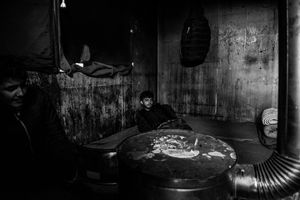 Refugee warms himself by the stove in temporary shelter at the back main train station in Belgrade, Serbia.