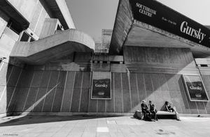 Tourists seated on a bench behind the Hayward Gallery on the South Bank, London | 02