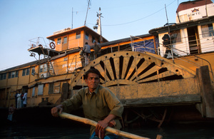 Man rowing with "Rocket" paddle steamer in background, Sadarghat, Old Dhaka, Bangladesh