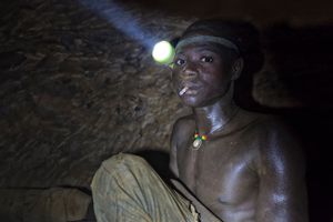 His "office" is a 50m deep, narrow, dangerous and claustrophobic pit. The air is thick, hot and humid, with constant dust that turns his dark arms and face white. He wears a flashlight strapped to his head as he chips ore from the walls into a spece he can barely sit up in. You can barely breathe down here, but for a break, Yakuba lights a cigarette. © Matjaz Krivic