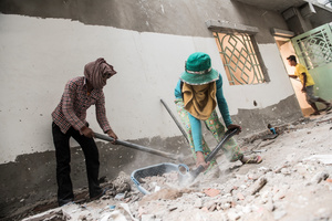 Two female workers clear up debris from the building site, many of the female workers are given menial tasks such as cleaning.