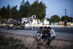Syrian Kurdish children from Kobane play with a cellphone outside the 'Arin Mirhan' refugee camp in the border town of Suruc, Sanliurfa province on November 10, 2014.