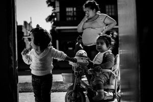 Stefi smokes a cigarette on the street in Monte Chingolo, while Maite and Mia play together. © Sarah Pabst