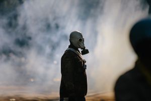 A protester wearing a gas mask walking through a cloud of tear gas fired during a stand-off between anti-Government protesters and police at Government House in Bangkok.