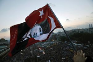 An anti-government protester waves a Turkish flag featuring Mustafa Kemal Ataturk, founder of modern Turkey, on the roof of the former Ataturk Cultural Center during a massive demonstration in Taksim Square in Istanbul, Turkey on Saturday June 8, 2013.